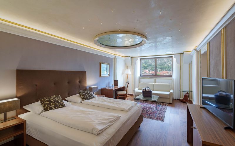 Modernes Hotelzimmer mit Doppelbett, Sofa, Schreibtisch und Fenster mit Bergblick