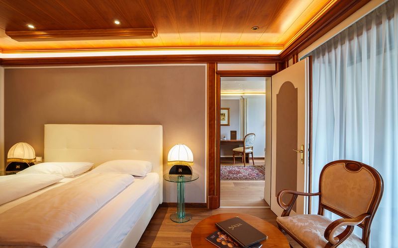 Elegantes Hotelzimmer mit Doppelbett, Nachttischlampen, Sessel und Holzmöbeln.