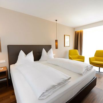 Modernes Doppelzimmer im Alpenstil mit gemütlichem Bett und Holzmöbeln im Hotel Vier Jahreszeiten